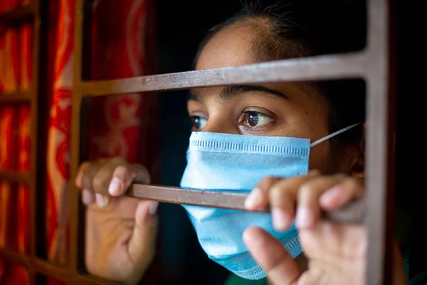Koronavirüs salgını sırasında evde karantina altında olan ve cerrahi maske takan sıkılmış Asyalı genç bir kız. Yakın plan görüntüler.