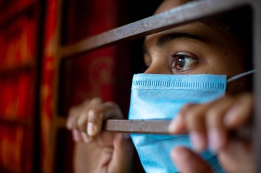 Koronavirüs salgını sırasında evde karantina altında olan ve cerrahi maske takan sıkılmış Asyalı genç bir kız. Yakın plan görüntüler.