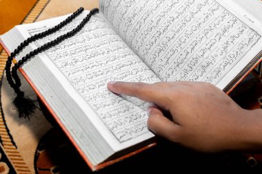 Müslüman kadın Kuran 'ı parmağıyla okuyor. Duaların üzerine Kur 'an-ı Kerim. Yakın çekim görüntüleri. İçeride. Ellere odaklan..