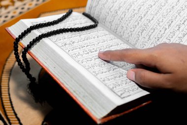 Müslüman kadın Kuran 'ı parmağıyla okuyor. Duaların üzerine Kur 'an-ı Kerim. Yakın çekim görüntüleri. İçeride. Ellere odaklan..