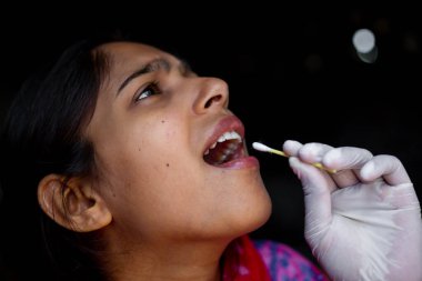 Doktorun eli, genç bayanın ağzından pamuklu çubukla tükürük testi alıyor. Coronavirus Gırtlak Koleksiyonu. Yakın plan görüntüler.