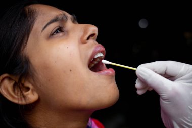 Doktorun eli, genç bayanın ağzından pamuklu çubukla tükürük testi alıyor. Coronavirus Gırtlak Koleksiyonu. Yakın plan görüntüler.