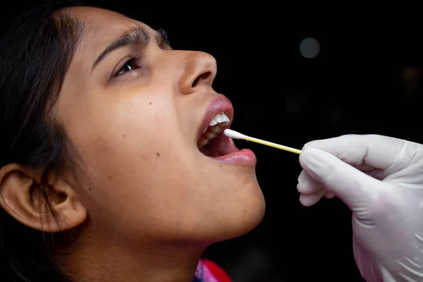 Doktorun eli, genç bayanın ağzından pamuklu çubukla tükürük testi alıyor. Coronavirus Gırtlak Koleksiyonu. Yakın plan görüntüler.