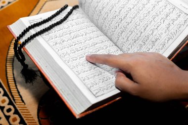 Müslüman kadın Kuran 'ı parmağıyla okuyor. Duaların üzerine Kur 'an-ı Kerim. Yakın çekim görüntüleri. İçeride. Ellere odaklan..