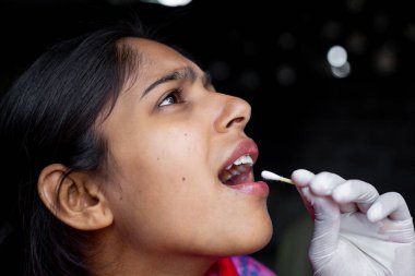 Doktorun eli, genç bayanın ağzından pamuklu çubukla tükürük testi alıyor. Coronavirus Gırtlak Koleksiyonu. Yakın plan görüntüler.