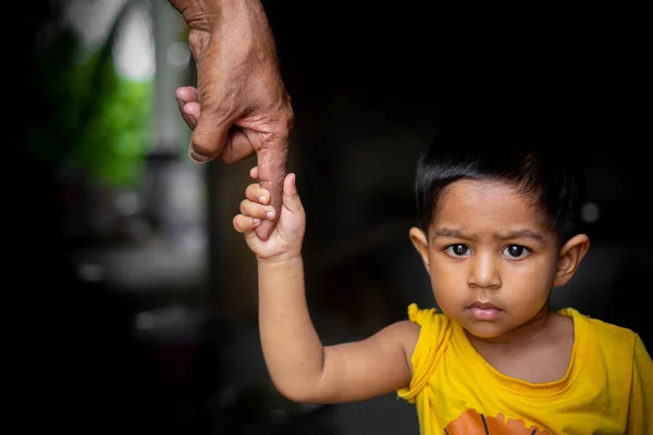 赤ん坊の少年は自信を持って老人の指を握って歩き回る 支援と人々の概念 暗い背景 — ストック写真