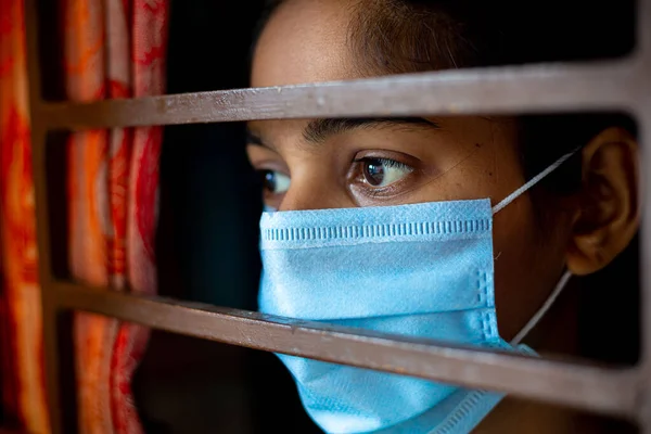 Koronavirüs salgını sırasında evde karantina altında olan ve cerrahi maske takan sıkılmış Asyalı genç bir kız. Yakın plan görüntüler.