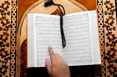 Müslüman kadın Kuran 'ı parmağıyla okuyor. Duaların üzerine Kur 'an-ı Kerim. Üst açı görüntüsü. Kapalı.