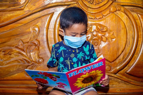 Ένα Αγοράκι Φοράει Μάσκα Προσώπου Και Κάθεται Στο Κρεβάτι Διαβάζοντας — Φωτογραφία Αρχείου