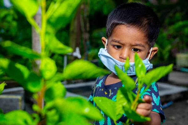 Tıbbi maske takan ve bahçede seyahat eden küçük bir çocuğun portresi. Ev karantinasındaki koronavirüs enfeksiyonundan koru..