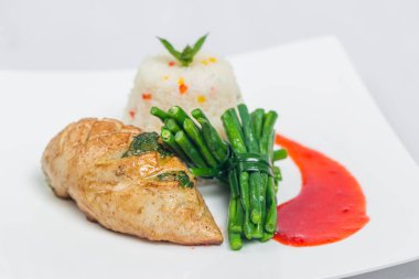 Tavada kızarmış tavuk göğsü, uzun yeşil fasulye ve hafif sebzeli pirinç tabağı. Beyaz tabakta kırmızı sosla süslenmiş yemek. İzole edilmiş beyaz arkaplan.