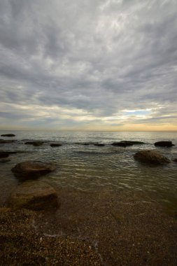 Sabahleyin Hazar Denizi kıyısında pembe-turuncu gökyüzü, gri bulutlar ve dalgalı deniz ve Kafkasya eteklerinde                               