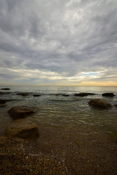 Sabahleyin Hazar Denizi kıyısında pembe-turuncu gökyüzü, gri bulutlar ve dalgalı deniz ve Kafkasya eteklerinde                               