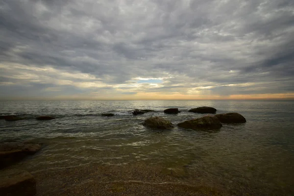 Kıyıda Hazar Denizi 'nin sabahı pembe-turuncu gökyüzü, dalgalar ve Kafkasların eteklerinde gri bulutlar                               