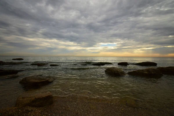 Hazar Denizi kıyısında sabah pembe-turuncu gökyüzü, gri bulutlar ve dalgalı deniz ve Kafkasya eteklerinde                              
