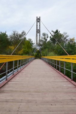Kuzey Kafkasya 'nın eteklerindeki Kizilovka Dağı' nda sarı korkuluklu ve gergin kablolarla asılı dağ köprüsünün manzarası.                               