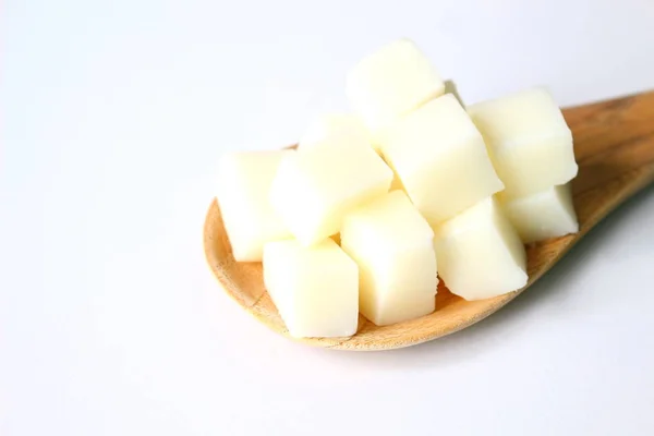 Close up of sliced white glycerin soap bases on wooden paddle on white background.