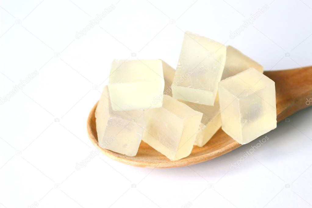 Sliced transparent glycerin soap bases, material for homemade soap, on wooden paddle on white background.