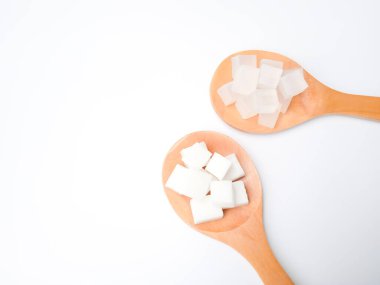 Beyaz arka planda iki tahta kaşık, her biri sabun tabanında kesilmiş küp taşıyor, beyaz ve şeffaf. Eritme ve gliserin sabun malzemelerinin üzerine röfle dök. Gliserin el yapımı cilt malzemesi için ideal..