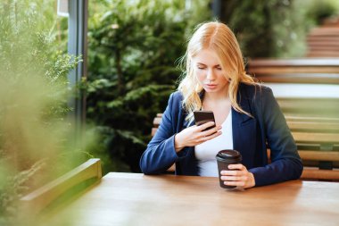 Restoran terasında, odaklanmamış bir geçmişi olan akıllı bir telefonla mesajlaşan kız.