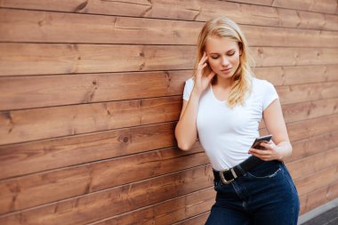 Çekici ahşap duvar arka plan ile kopyalama alanı alanı, cep telefonu ile gülümseyen ve sevinç içinde çok mutlu hissediyorum seyir hipster oldukça raslantı giyimli kadın ayakta kadın gülüyor