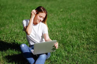 Kadın sit n park dizüstü bilgisayar ile yeşil çimenlerin üzerinde defter, eller klavye üzerinde. . Öğrenci açık havada.