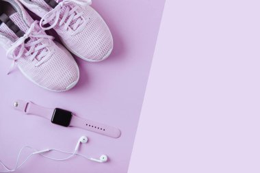 Violet spor ayakkabıları, kulaklıklar ve saatler. Düz stil pembe arkaplan.