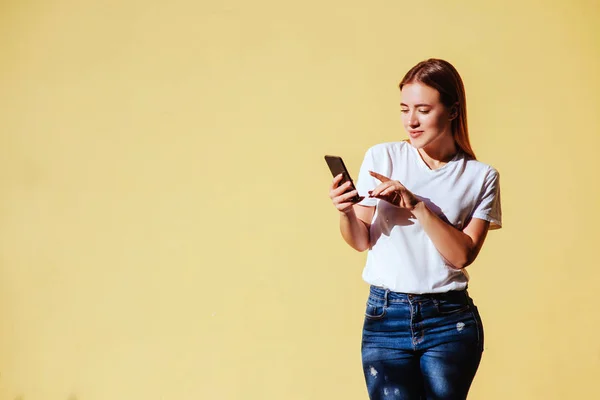 Portrait Smiling Beautiful Blonde Girl White Shirt Jeans Smartphone Yellow — Stock Photo, Image