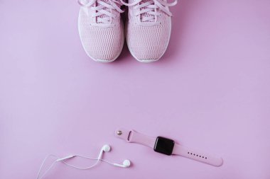 Violet spor ayakkabıları, kulaklıklar ve saatler. Düz stil pembe arkaplan.