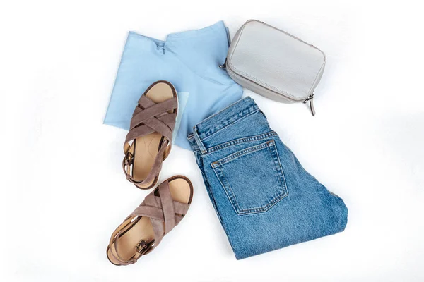 Stylish female clothes set. Girl outfit on white background. Blue jeans, bag, t-shirt, sandals. Flat lay, top view
