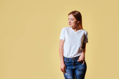 Beyaz t-shirt ve jeans sarı arka plana karşı gülümseyen güzel sarışın kız portresi.