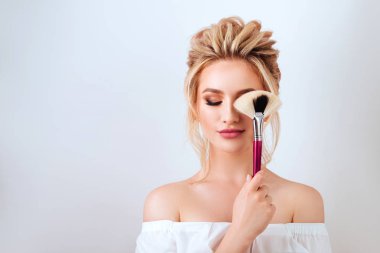 Moda glamour fırça ışık stüdyo arka plan üzerinde tutan mutlu gülümseyen sarışın kadın uzun dalgalı saç stili portresi. Güzel yüzlü yapmak kadar ürün kozmetik.