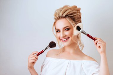 Moda glamour fırça ışık stüdyo arka plan üzerinde tutan mutlu gülümseyen sarışın kadın uzun dalgalı saç stili portresi. Güzel yüzlü yapmak kadar ürün kozmetik.