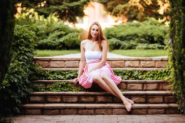 Çekici genç bir kadın, arka planda günbatımıyla parkta eğleniyor..