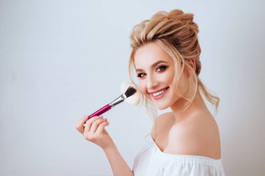 Moda glamour fırça ışık stüdyo arka plan üzerinde tutan mutlu gülümseyen sarışın kadın uzun dalgalı saç stili portresi. Güzel yüzlü yapmak kadar ürün kozmetik.