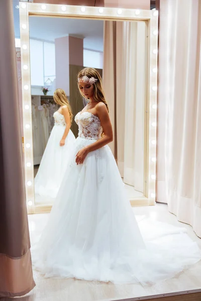 美しい花嫁は モダンなウェディング サロンで優雅なウェディング ドレスを試着します — ストック写真