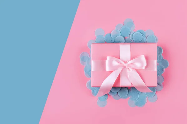 Present box with pink bow on pastel pink background.