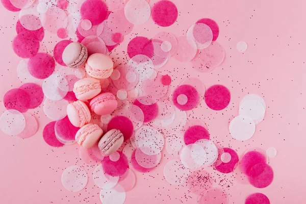 Chutné barevné macarons na módní pastelově růžovém papíře s konfety. — Stock fotografie