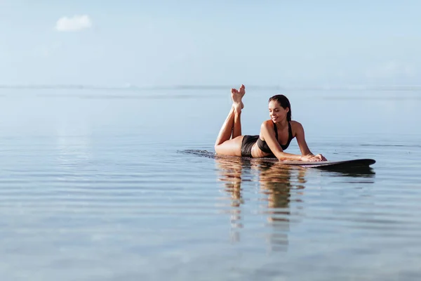 Женщина улыбается и сидит на доске для серфинга в океане . — стоковое фото