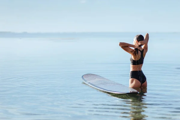 Mulher sorri e senta-se na prancha de surf no oceano . — Fotografia de Stock