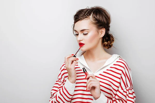 Молодая женщина с красными губами на довольно эмоциональное лицо в элегантном платье держа помаду макияж в студии — стоковое фото
