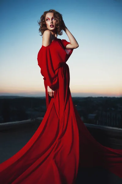 Moda estilo moda retrato de mujer joven impresionante posando en vestido rojo en la puesta del sol — Foto de Stock