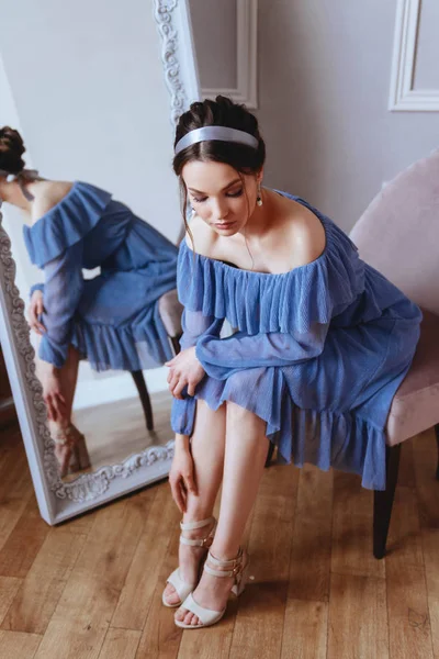 Una hermosa mujer en un vestido azul está sentada en un sillón de terciopelo — Foto de Stock