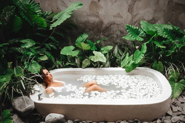 Mulher relaxante em banho redondo ao ar livre com flores tropicais, cuidados com a pele orgânicos — Fotografia de Stock