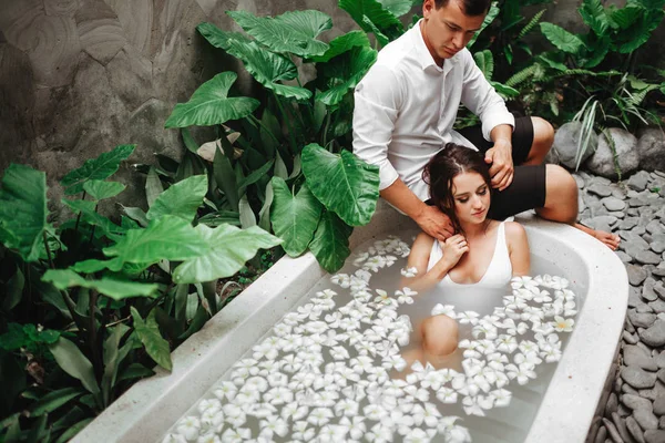 Frau und Mann entspannen sich in einem Bad mit tropischen Blumen im Freien eines Luxushotels. — Stockfoto