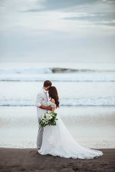 Elegante linda noiva e noivo andando na praia do oceano durante o pôr do sol . — Fotografia de Stock