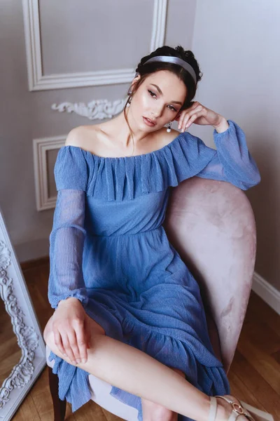 Una hermosa mujer en un vestido azul está sentada en un sillón de terciopelo — Foto de Stock