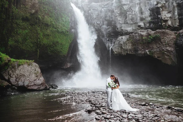 Pareja joven enamorada novia y novio, día de la boda cerca de una cascada de montaña . —  Fotos de Stock