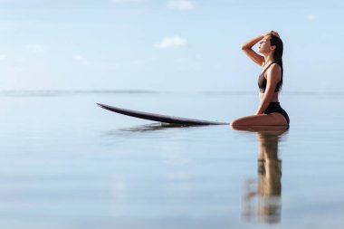 Kadın gülümsüyor ve okyanus sörf tahtası üzerinde oturur.