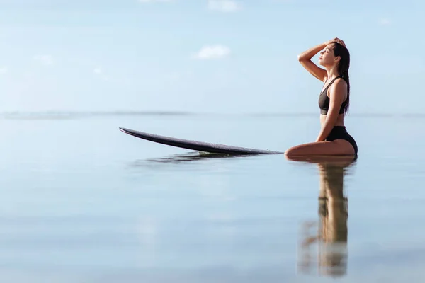 Mulher sorri e senta-se na prancha de surf no oceano . — Fotografia de Stock